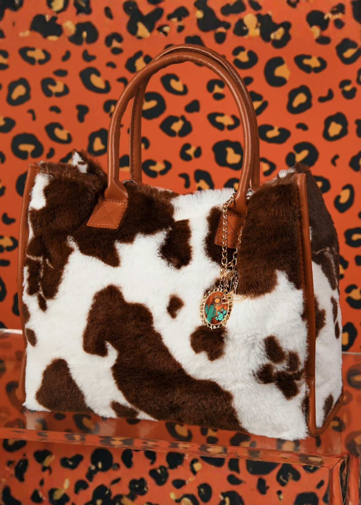 Brown and white cowhide patterned bag with a decorative tag against a leopard print background