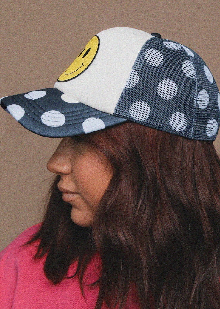 Person wearing a cap with a smiley face design on a beige background