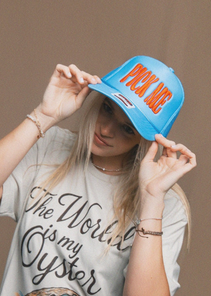 Person wearing a blue cap with 'Pick Me' text and a white t-shirt with 'The World is my Oyster' text.