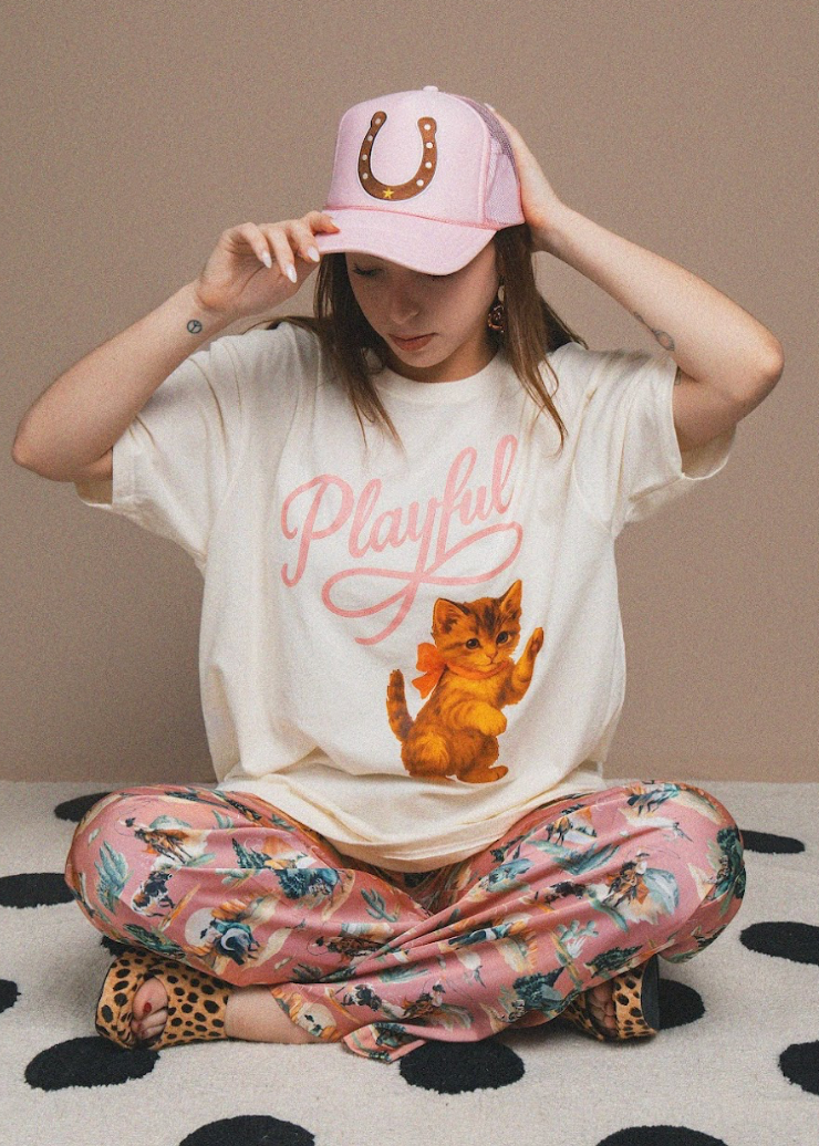 Person wearing a white t-shirt with a cat graphic and 'Playful' text, sitting on a polka dot surface.