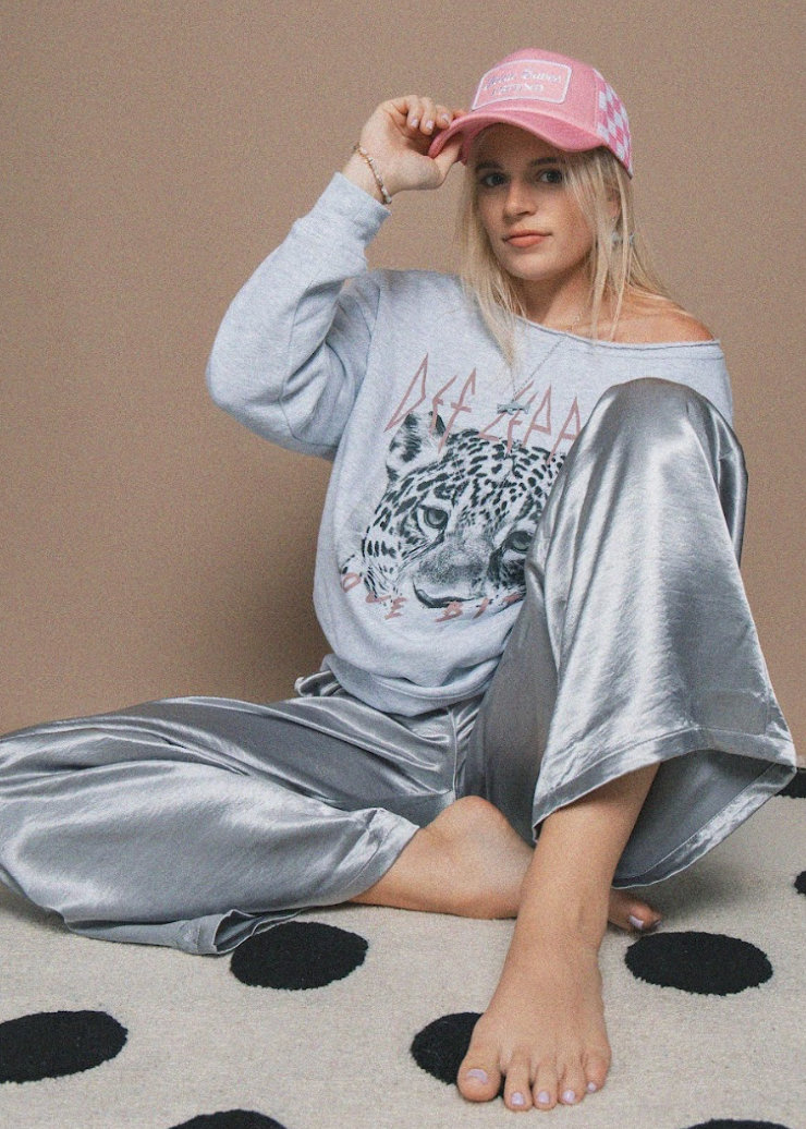 Woman wearing a gray sweatshirt with a leopard print and silver pants, sitting on a polka dot surface.