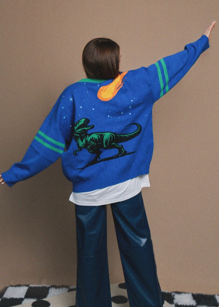 Person wearing a blue sweater with a dinosaur design on a brown background