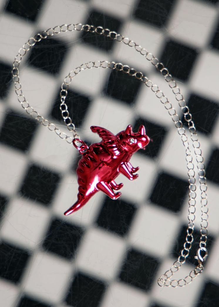 Red dinosaur pendant on a silver chain against a black and white checkered background