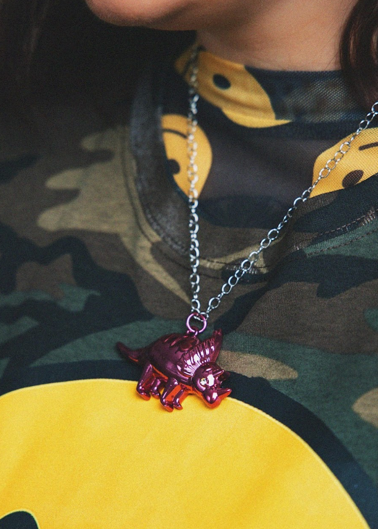 Necklace with a red and purple pendant worn by a person in camouflage clothing.