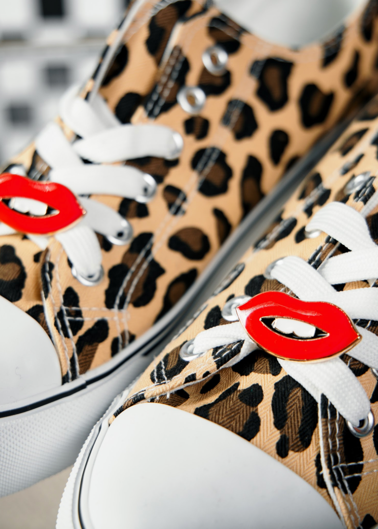 Leopard print sneakers with red lip shoe clips on white laces against a blurred background