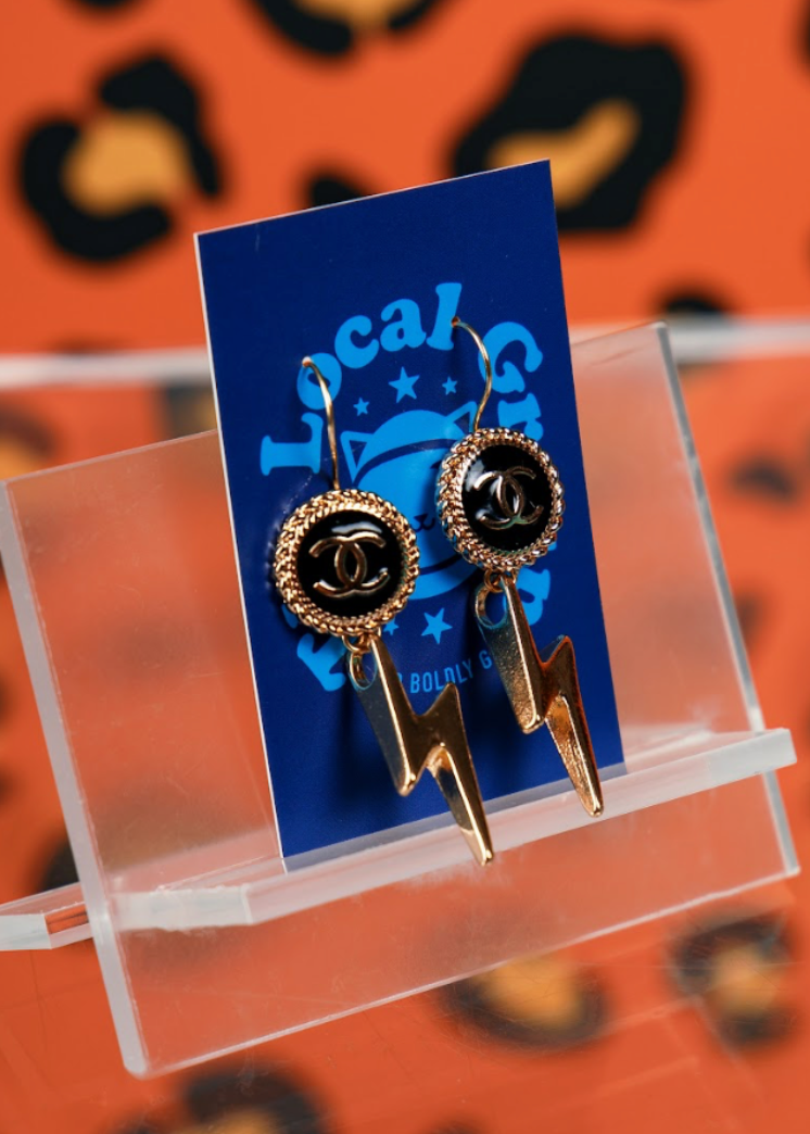 Gold earrings on a clear stand with a blue card against an orange background