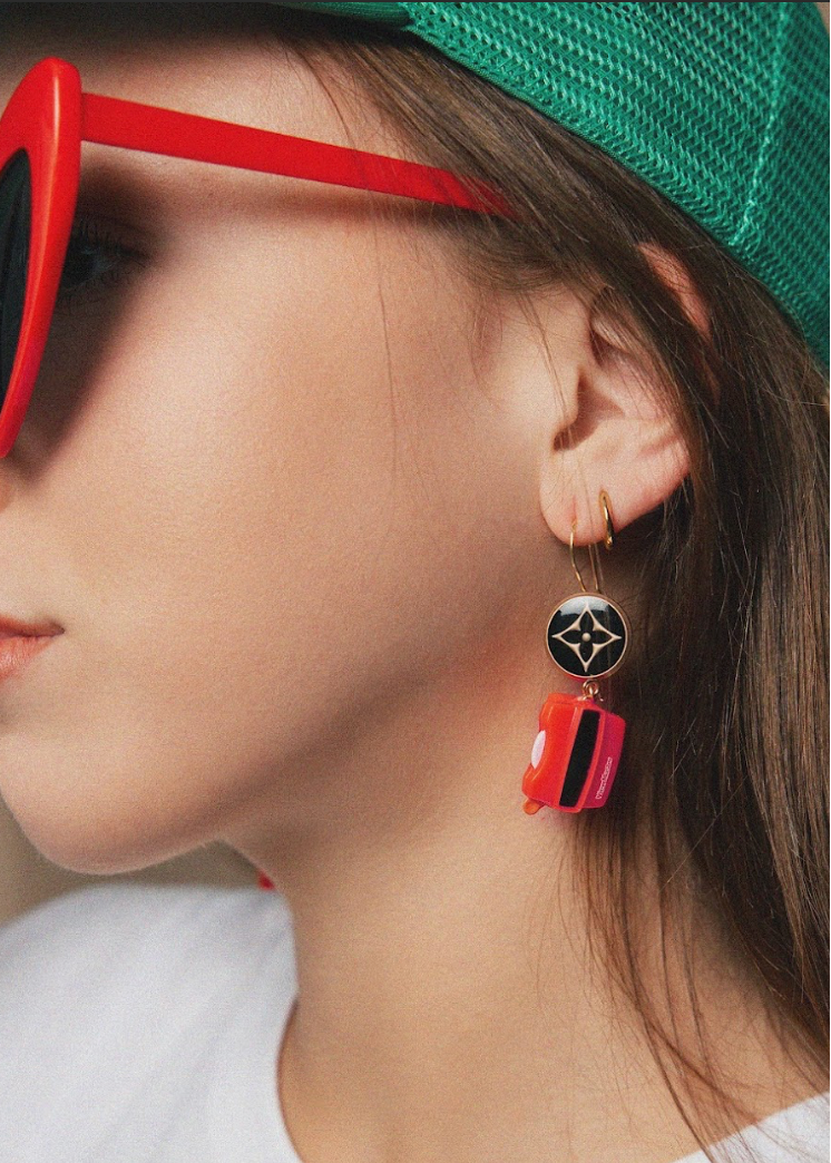 Close-up of a person wearing heart-shaped red sunglasses and colorful earrings.