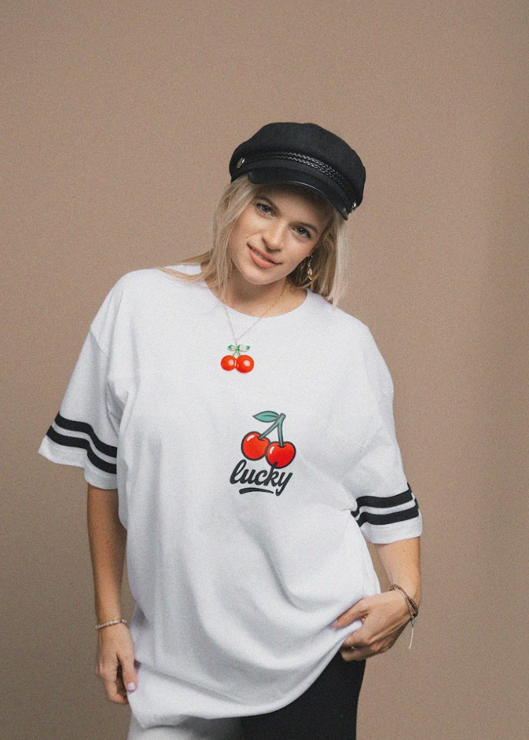 Person wearing a white t-shirt with cherry design and 'lucky' text on a brown background