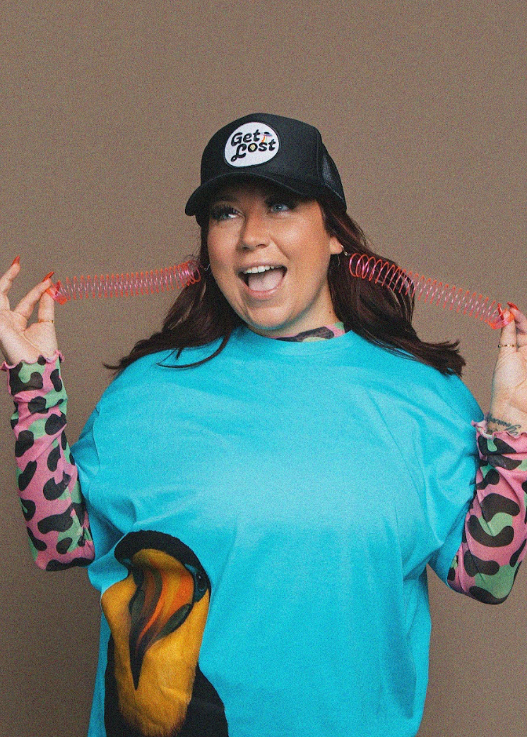 Person wearing a blue sweater and colorful sleeves with a black cap, holding pink spiral earrings.
