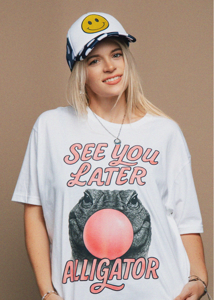 Person wearing a white t-shirt with 'See You Later Alligator' graphic and a cap with a smiley face design.