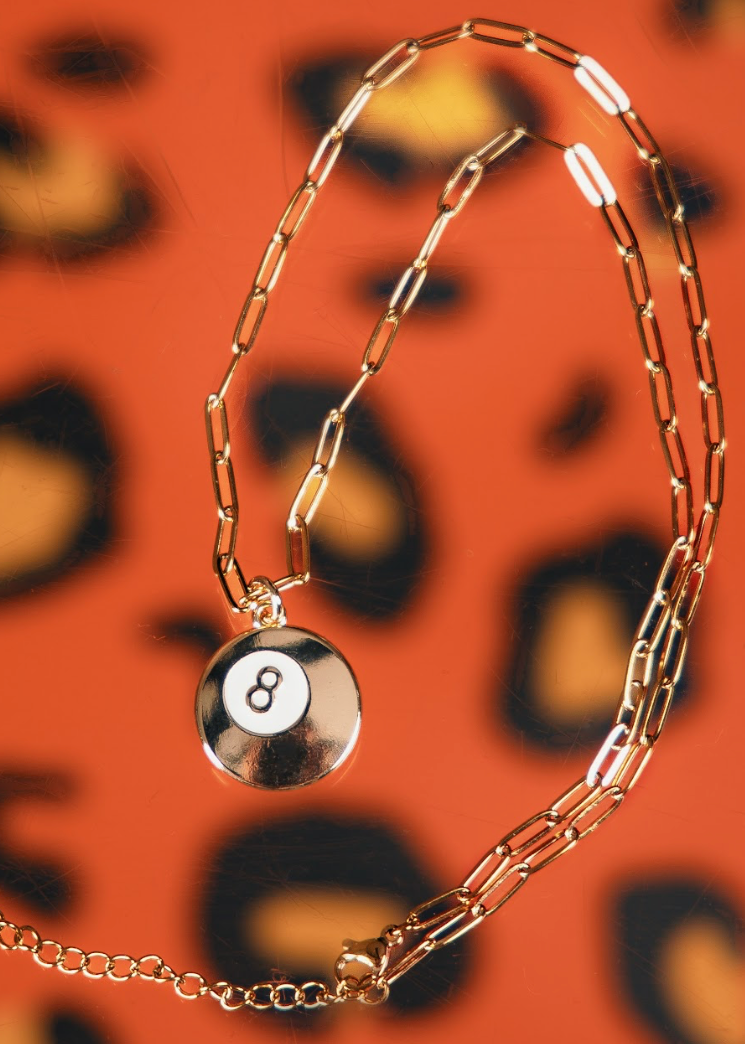 Gold chain bracelet with a round charm featuring the number 8 on an orange background.