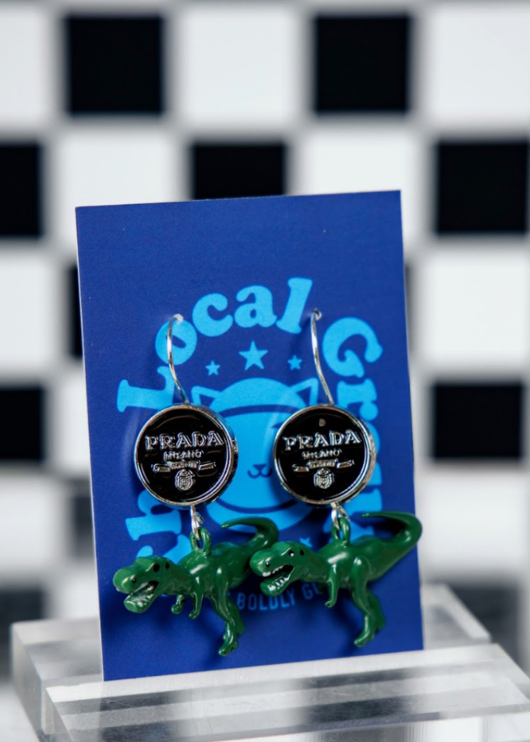 Dinosaur-shaped earrings on a blue card with a checkered background