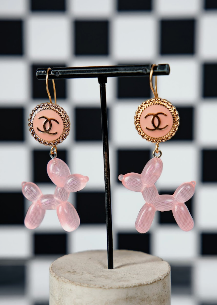 Pink dog-shaped earrings with Chanel logo on a black and white checkered background