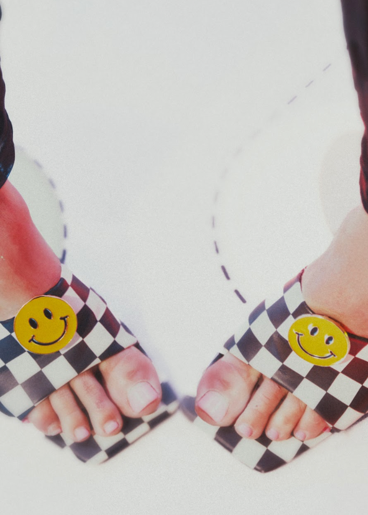 Checkered mule sandals with smiley face clips against a white background