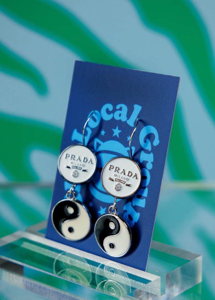 Prada earrings on a blue card with 'Local Group' branding against a green and white abstract background.