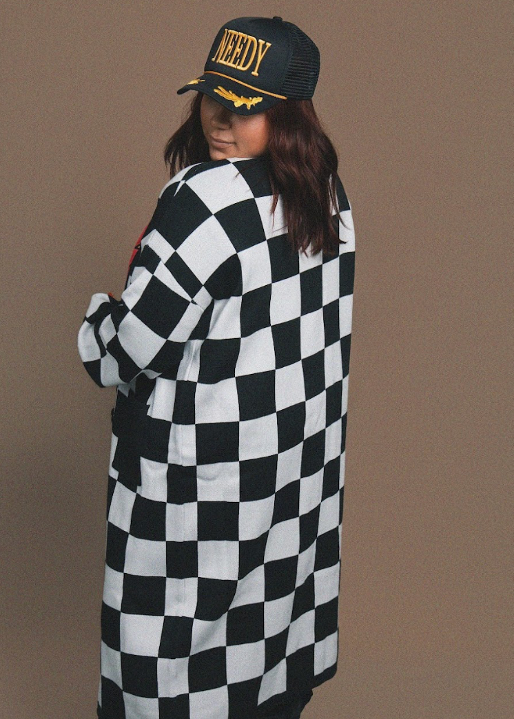 Person wearing a black and white checkered cardigan with a cap on a brown background