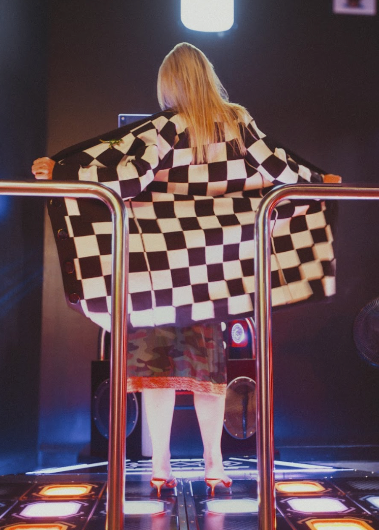 Person wearing a checkered cardigan standing on a stage with a spotlight.
