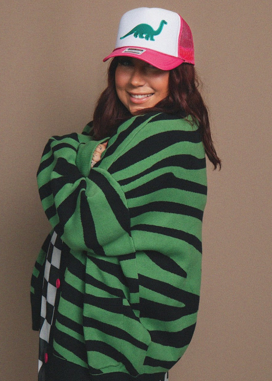 Person wearing a green and black striped sweater and a red and white cap with a dinosaur design on a beige background