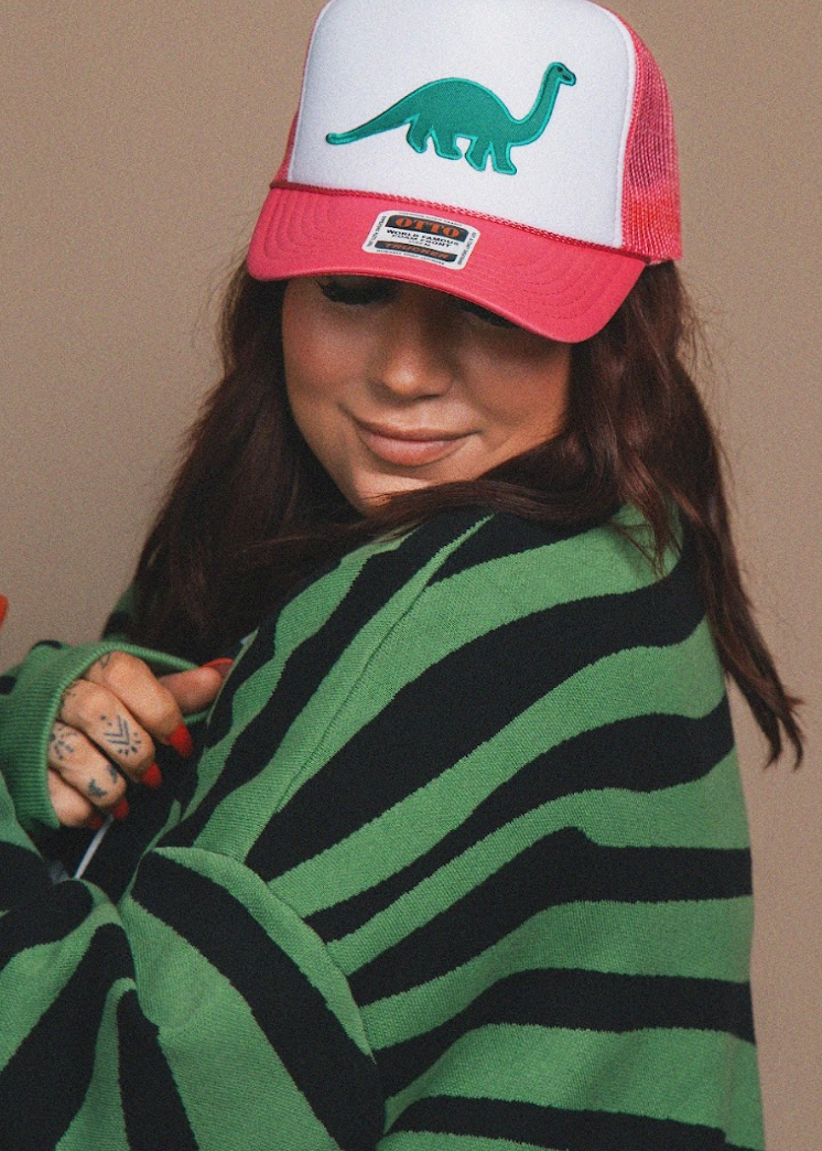Person wearing a green and black striped sweater and a cap with a dinosaur design on a beige background
