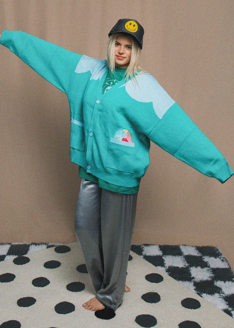 Person wearing a teal cardigan with cloud designs on a checkered floor.