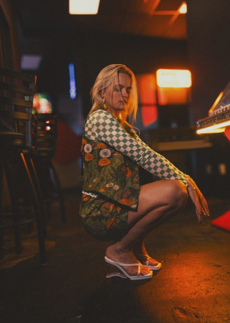Woman sitting on a bar stool in a dimly lit bar with floral-patterned jacket.