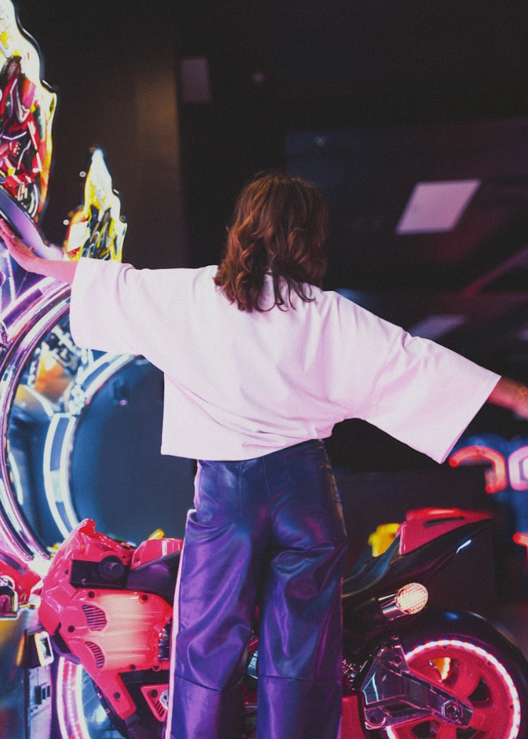 Person in white tee standing in arcade with colorful lights and graphics.