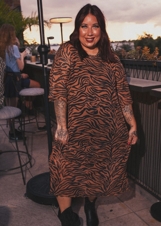 Woman in a tiger print dress standing in an outdoor setting with tables and chairs.