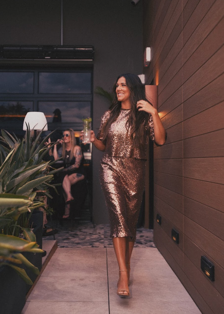 Woman in a sparkly dress walking outdoors with people in the background.