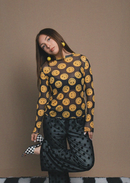 Woman wearing a patterned top and black skirt against a brown background