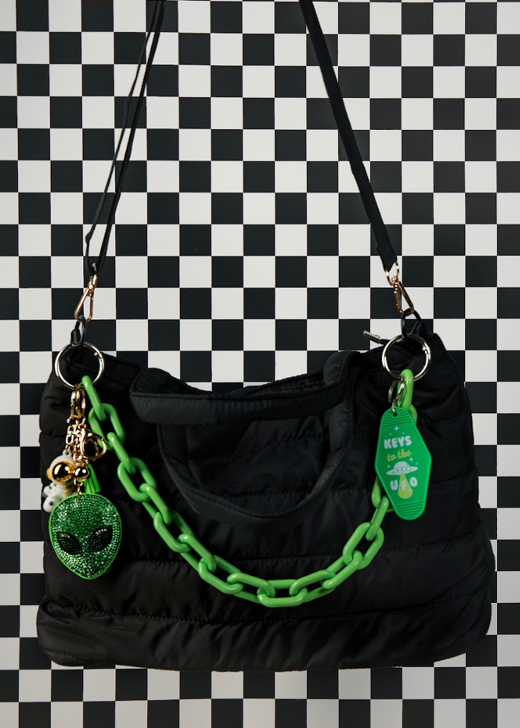 Black handbag with green chain and alien charm on a checkered background