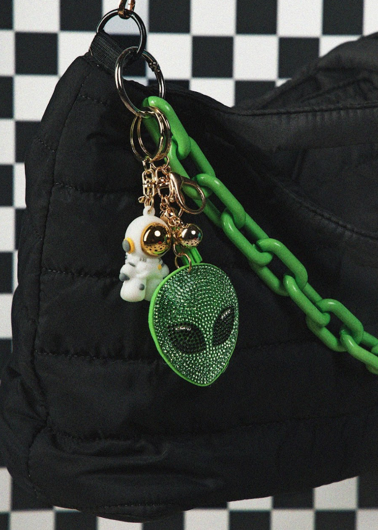 Keychain with alien charm and green chain on a black bag against a checkered background