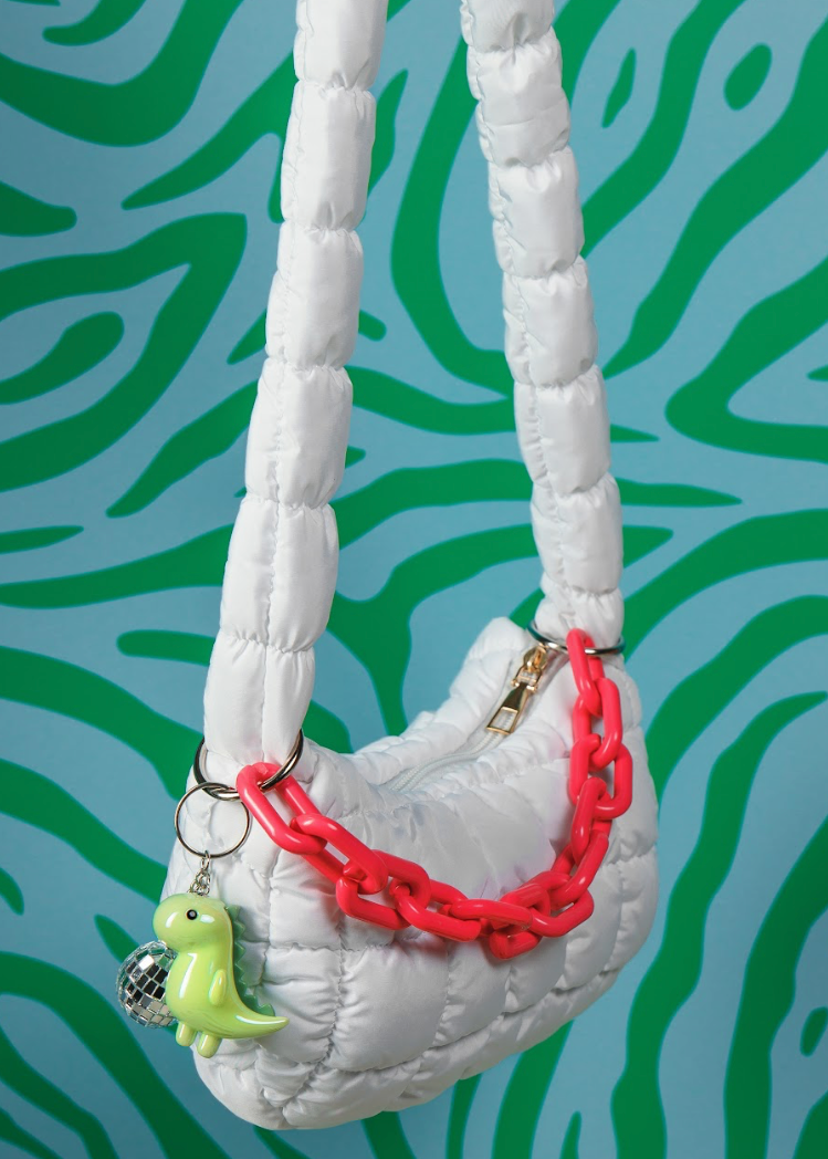 White quilted handbag with red chain and green charm against a green and blue patterned background