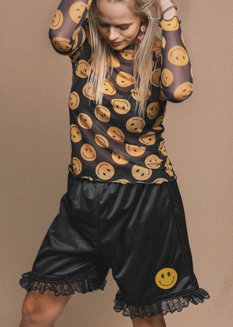 Person wearing a black outfit with smiley face patterns on a beige background