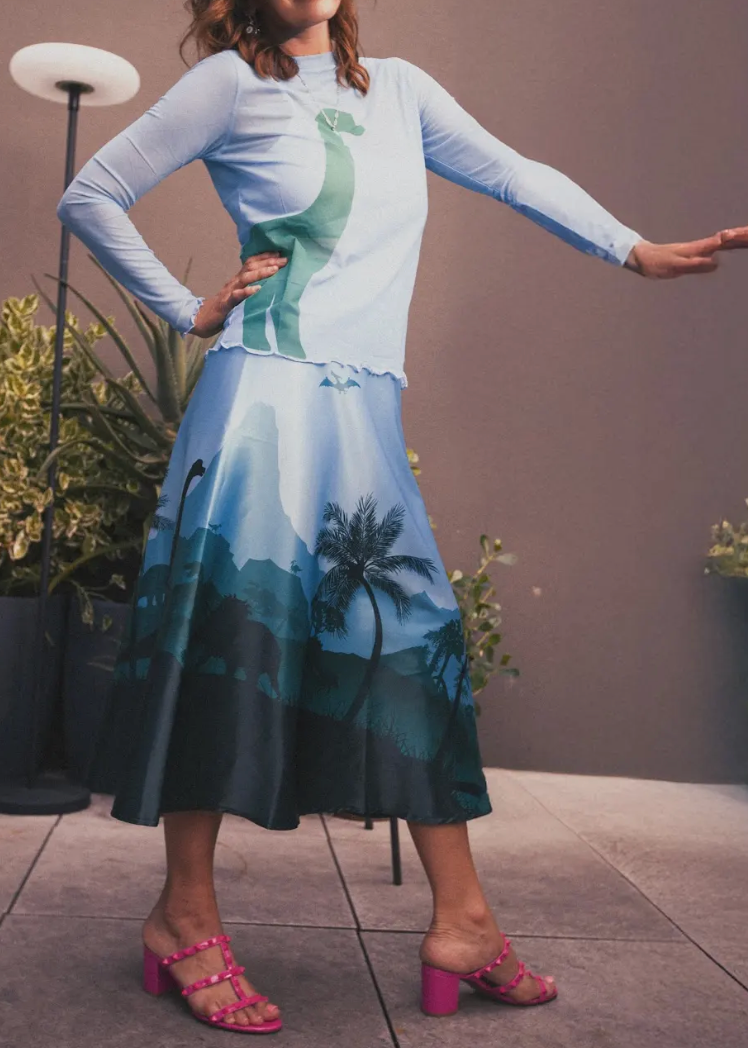 Woman wearing a long-sleeve top and skirt with nature-themed design, standing indoors.