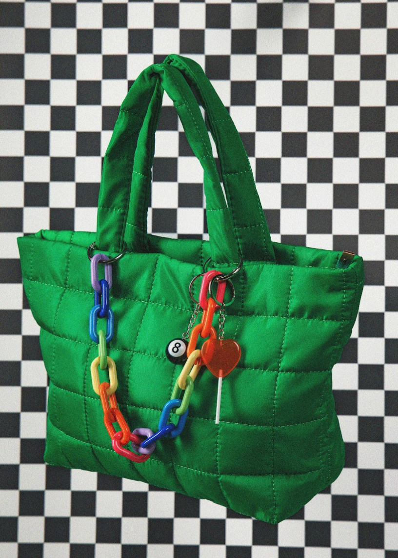 Green quilted handbag with colorful chain and keychain on a black and white checkered background