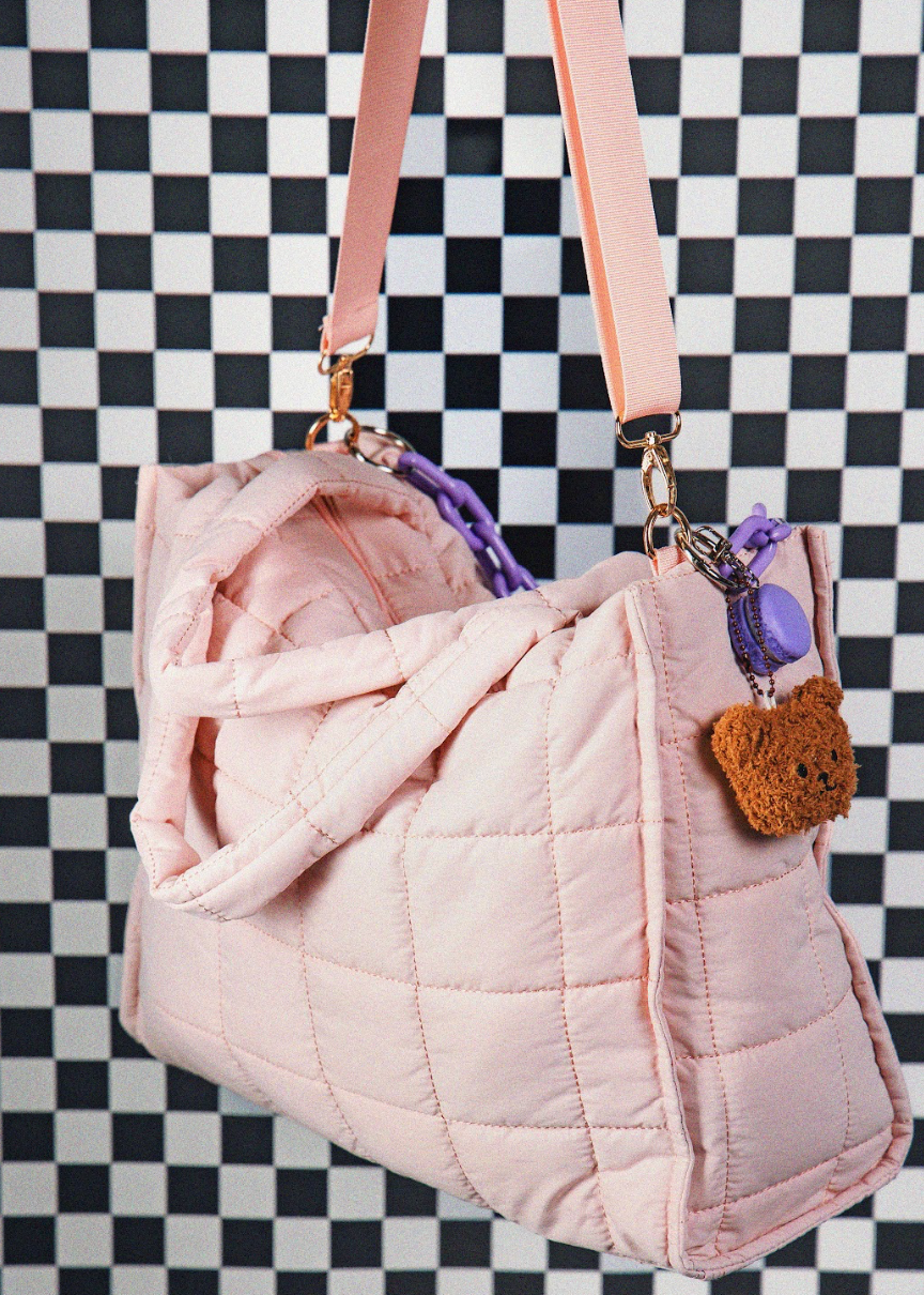 Pink quilted handbag with a strap and decorative charm on a checkered background