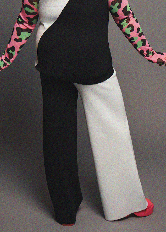 Person wearing a black top and white pants with colorful sleeves on a gray background