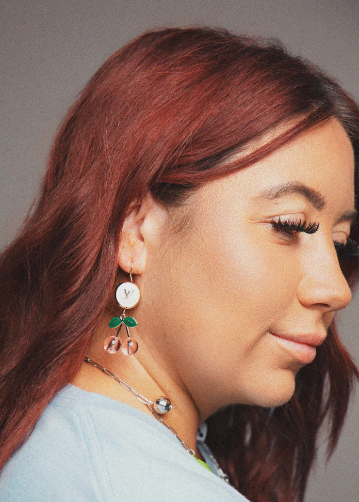 Close-up of a person with long hair wearing earrings and a necklace against a neutral background