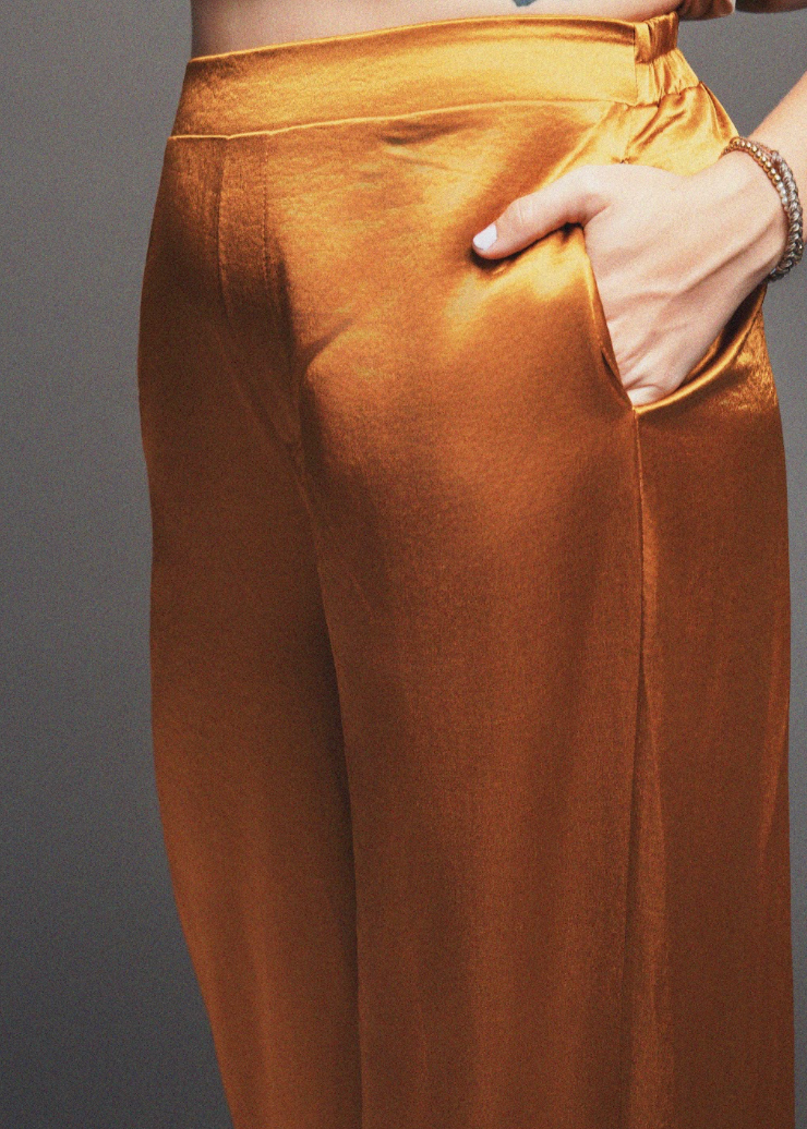 Gold satin pants with a hand in the pocket against a gray background