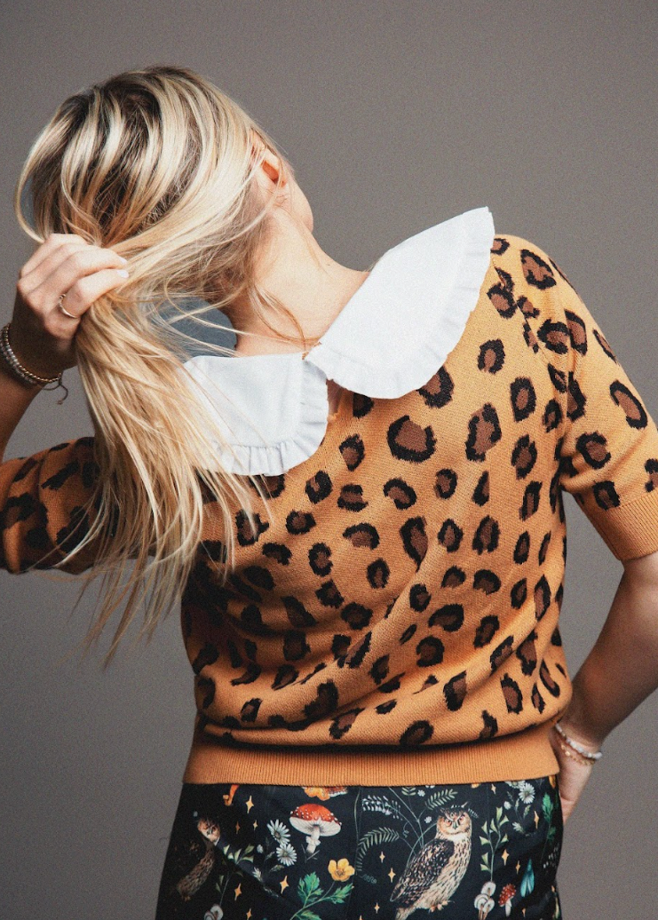 Person wearing a leopard print sweater with a white collar against a gray background