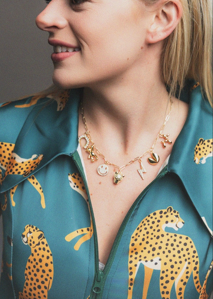 Woman wearing a gold necklace with various pendants against a neutral background
