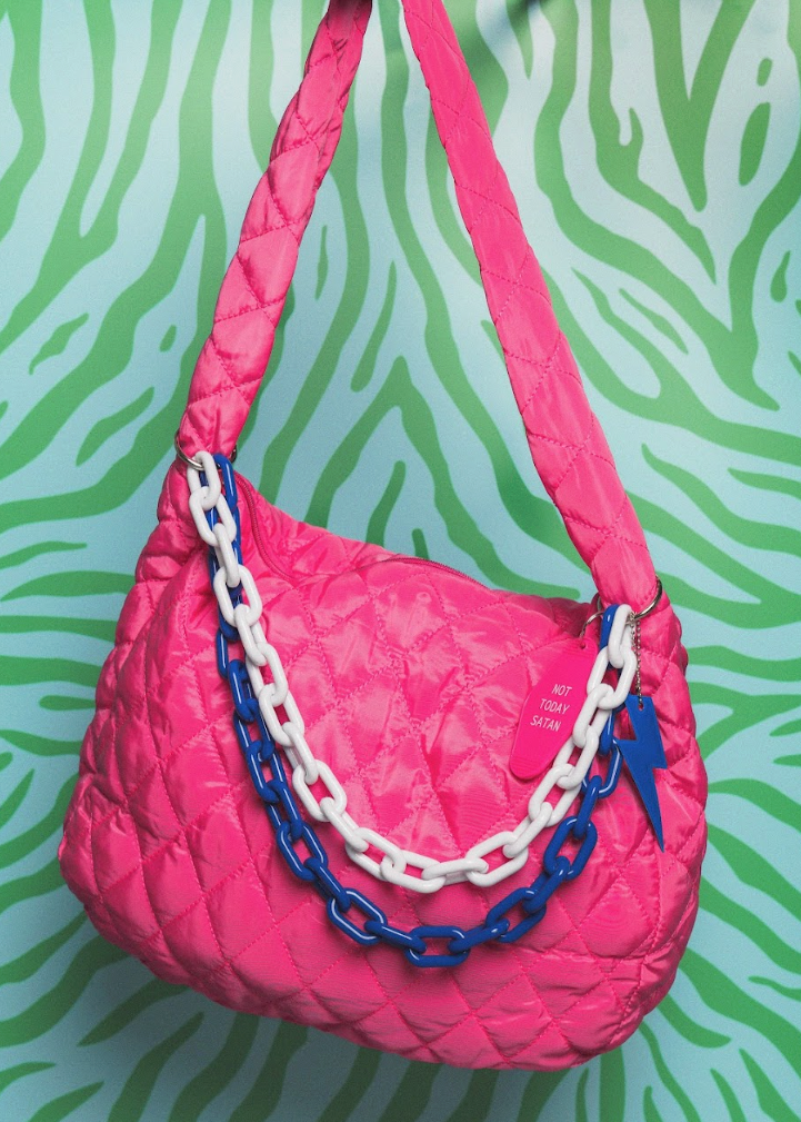 Pink quilted handbag with blue and white chain details on a green and white zebra pattern background