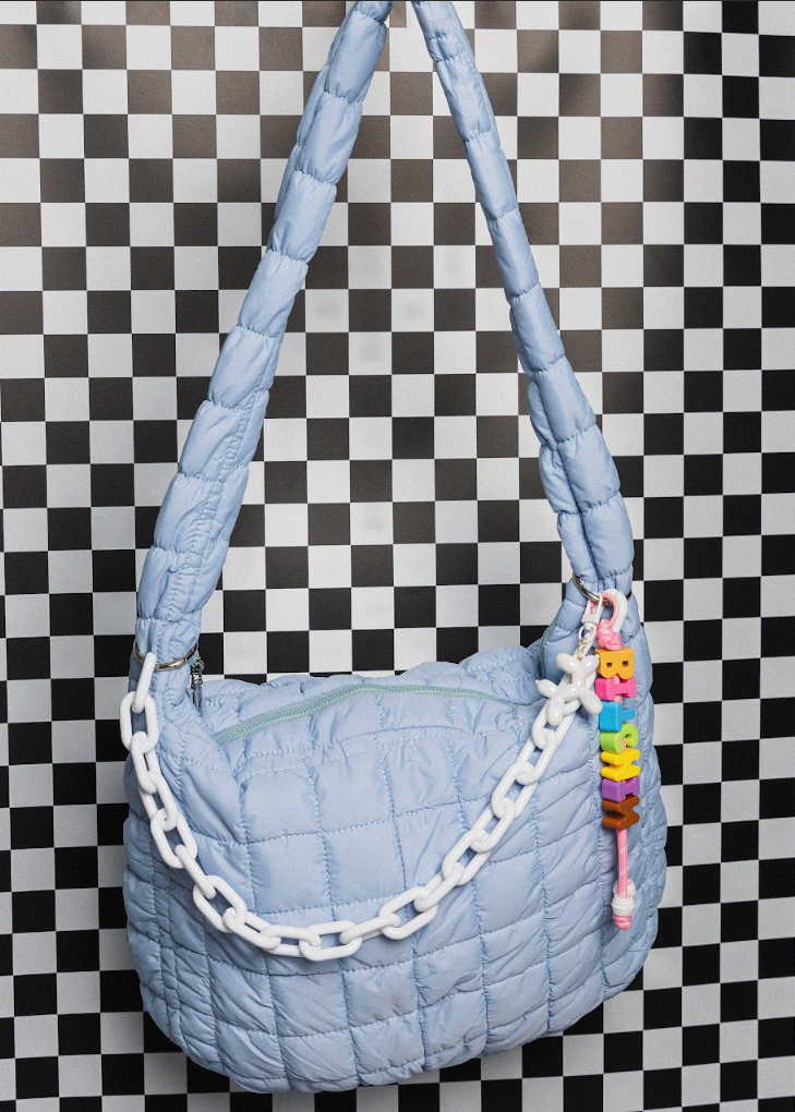 Light blue quilted handbag with colorful chain detail on a checkered background
