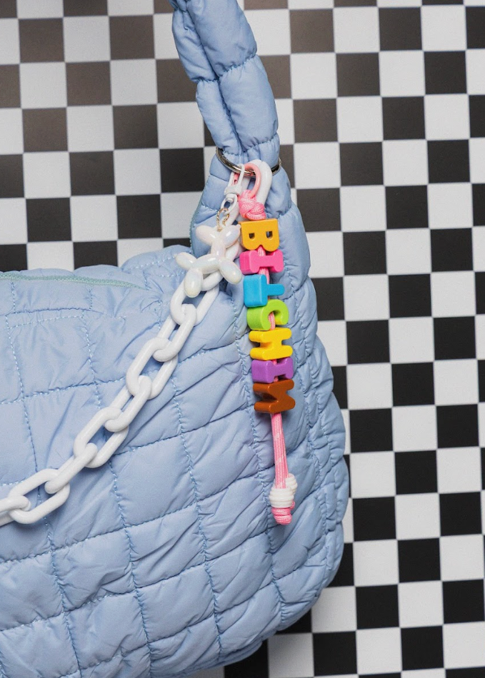 Blue quilted handbag with a colorful "BITCHIN" charm on a checkered background