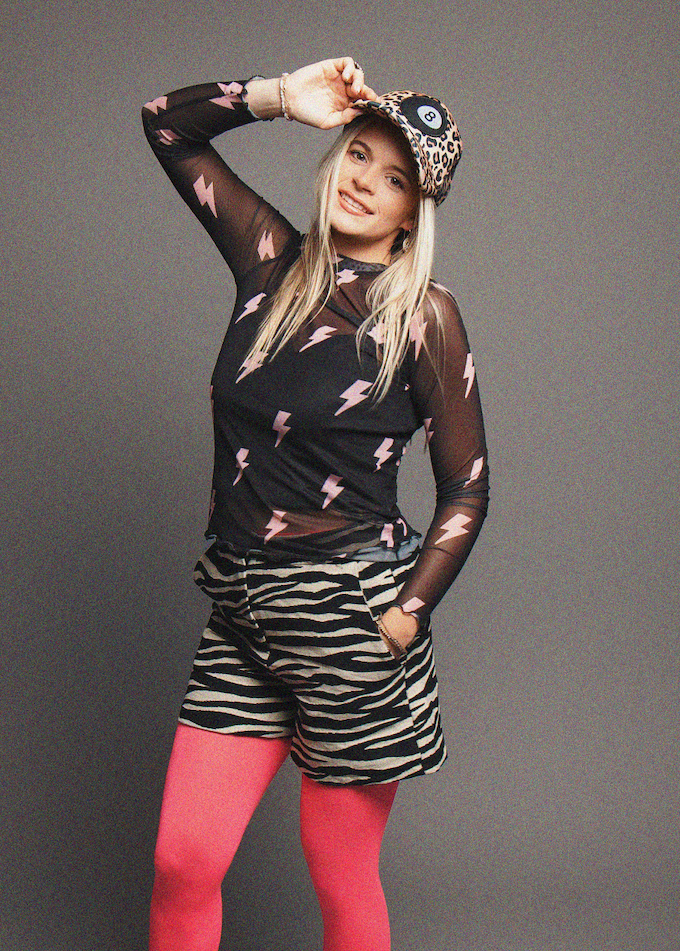 Person wearing a black sheer top with pink designs, zebra print shorts, and red tights on a gray background