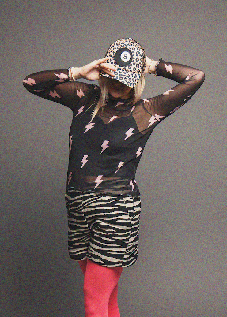 Person wearing a black sheer top with pink lightning bolts and zebra print shorts on a gray background