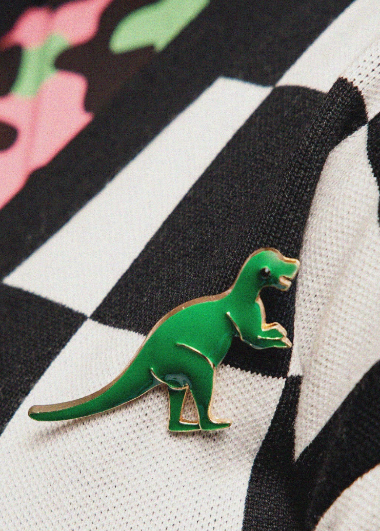 Green dinosaur pin on a black and white striped fabric background