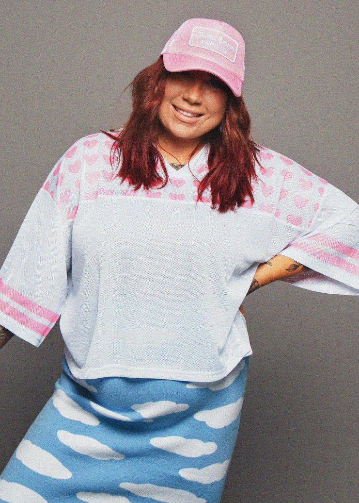 Person wearing a light blue and pink outfit with a pink cap against a gray background