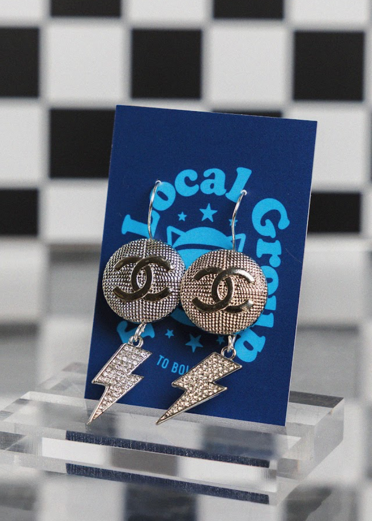 Chanel earrings with lightning bolt designs on a blue card with 'Local Grocer' branding against a checkered background.