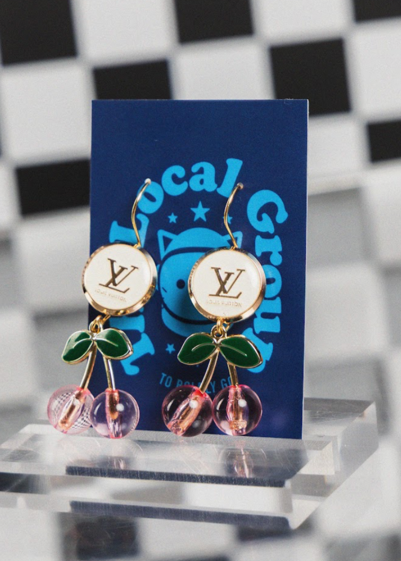 Cherry-themed earrings on a blue card with visible brand logo against a checkered background